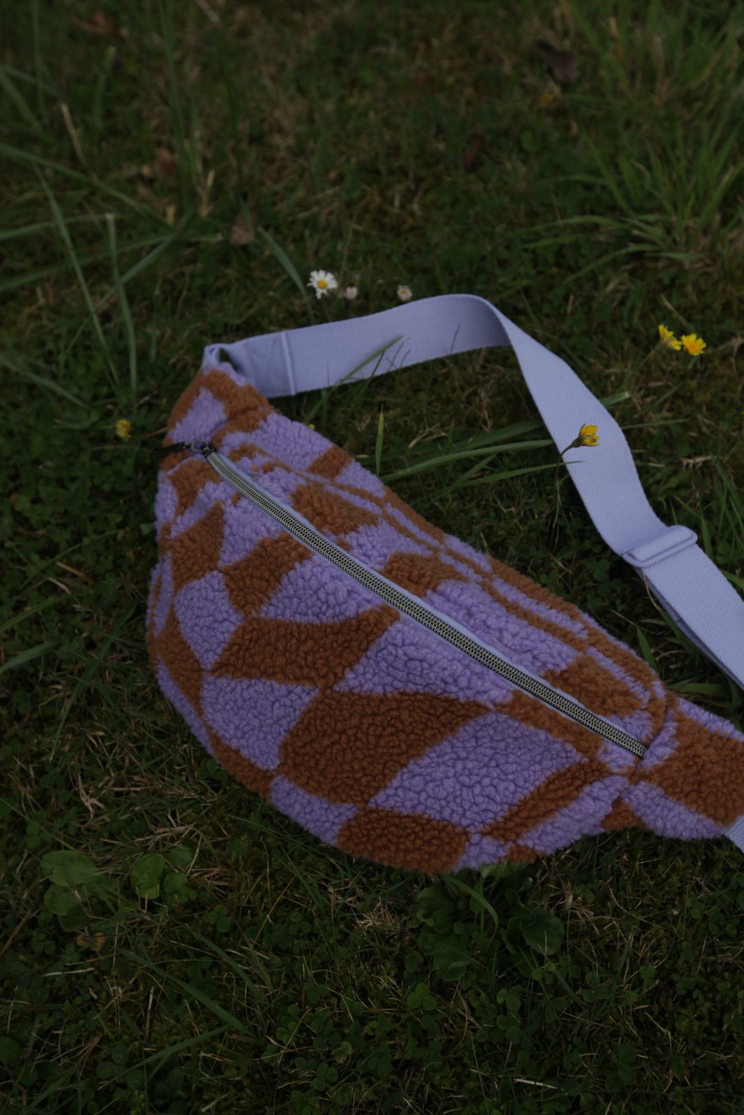 Teddy-Umhängetasche in Flieder und Rostrot im Gras liegend
